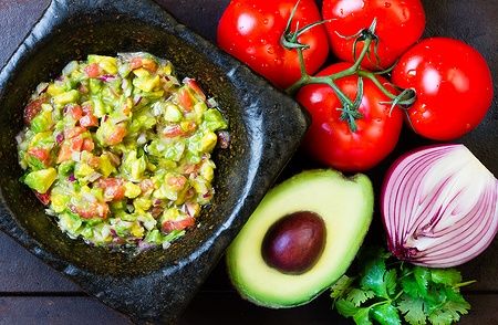 Guacamole in mortaio di pietra con pomodori, avocado, cipolla e coriandolo.