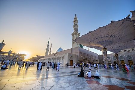 Tramonto sulla Moschea del Profeta a Medina con fedeli che pregano sotto il cielo dorato.