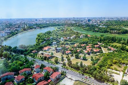 Vista aerea del Parco Herăstrău e del lago a Bucarest, circondato da vegetazione e abitazioni.