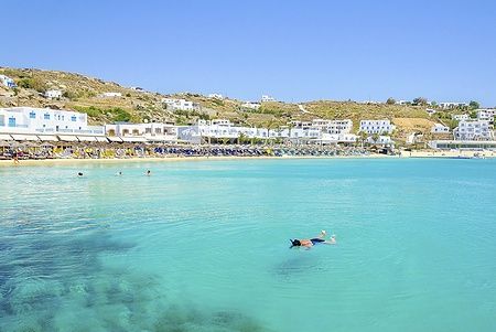 Spiaggia di Platis Gialos a Mykonos, donna in snorkeling e case bianche.