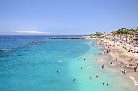 Spiaggia sabbiosa di Playa del Duque a Costa Adeje, Tenerife, con persone che nuotano.
