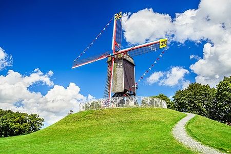 Mulino a vento Sint Janshuismolen su collina verde a Bruges sotto cielo blu.