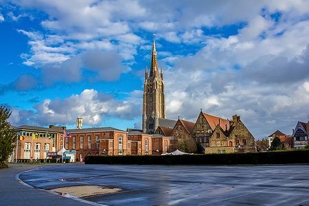La torre della Chiesa di Nostra Signora a Bruges sotto un cielo blu con nuvole.