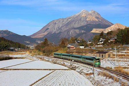 Treno tra i campi innevati con una montagna sullo sfondo a Yufuin, Giappone.