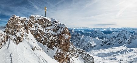 Panorama invernale dalla cima dello Zugspitze con neve e croce dorata.