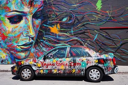 Auto dipinta con graffiti davanti a un murale colorato a Wynwood, Miami.