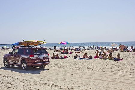 Veicolo dei bagnini sulla spiaggia di Mission Bay a San Diego con persone e ombrelloni colorati.