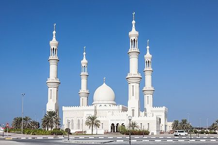 Moschea bianca di Ajman con minareti sotto il cielo azzurro.