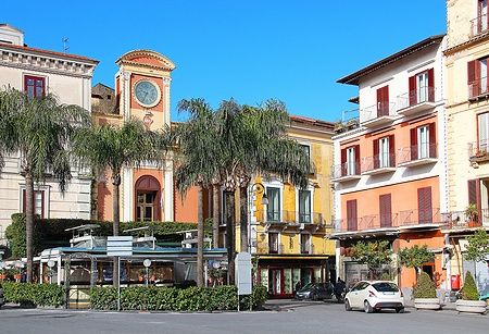 Piazza Tasso a Sorrento con edifici colorati e palme sotto un cielo azzurro.