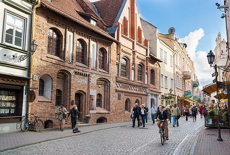 Pilies Street a Vilnius con persone che camminano e un uomo in bicicletta.