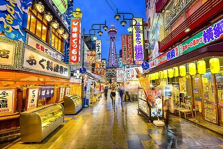 Folla cammina nel distretto Shinsekai di Osaka sotto le luci notturne.