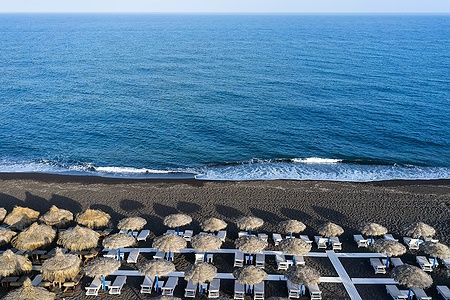 Spiaggia di Perissa a Santorini con ombrelloni e mare blu.