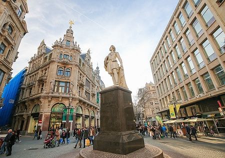 Statua di Anthony Van Dyck sulla strada Meir ad Anversa, Belgio, con persone e edifici storici.