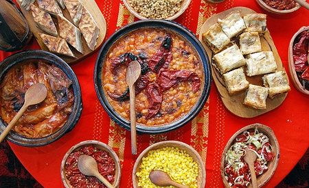 Cibo tradizionale macedone e balcanico disposto su una tovaglia rossa.