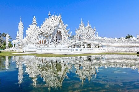 Il Tempio Bianco di Chiang Rai riflesso in un lago sotto un cielo blu.