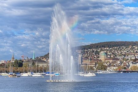 Fontana sul lago di Zurigo con arcobaleno e skyline della città sullo sfondo.