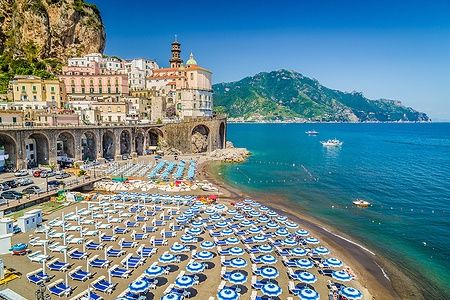 Spiaggia di Atrani sulla Costiera Amalfitana con ombrelloni blu e bianchi.