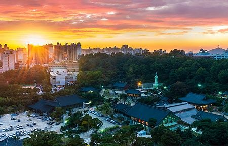 Tempio Bongeunsa a Seoul illuminato al tramonto con la città sullo sfondo.