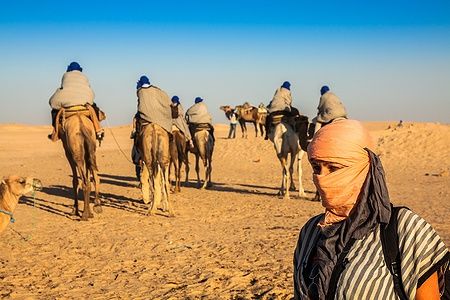 Beduini guidano turisti su cammelli nel deserto di Douz, Tunisia.