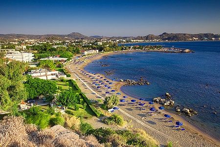 Vista della spiaggia di Faliraki con ombrelloni blu e mare cristallino a Rodi.