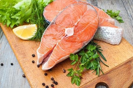 Fette di salmone crudo con erbe fresche su tagliere di legno.