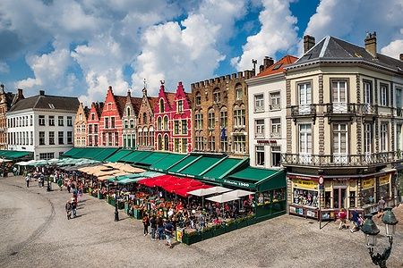 Grote Markt di Bruges con caffè all'aperto e edifici storici colorati.