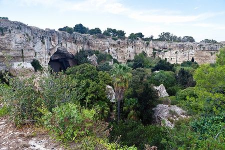 La Latomia del Paradiso a Siracusa con grotte e vegetazione lussureggiante.