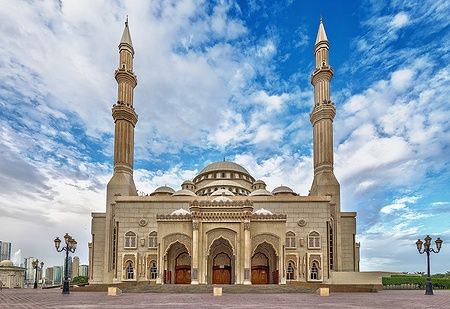 Moschea con due minareti a Sharjah, sotto un cielo azzurro e nuvoloso.
