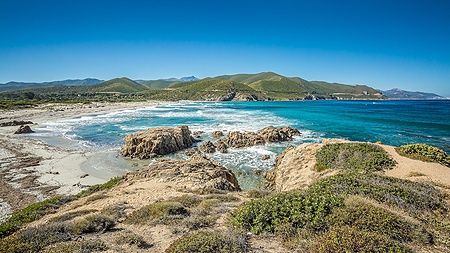 La spiaggia di Ostriconi in Corsica con mare blu e colline verdi.