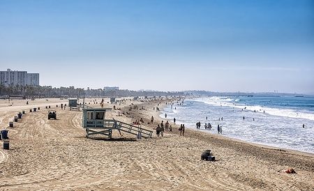 La spiaggia di Santa Monica affollata di bagnanti e surfisti sotto un cielo limpido.