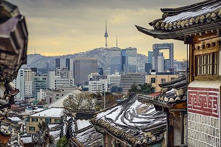 Veduta dei tetti innevati di Bukchon Hanok con la skyline di Seoul sullo sfondo.