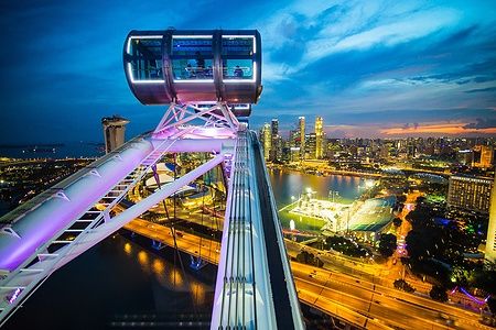 Vista notturna del Singapore Flyer e dello skyline illuminato al tramonto.