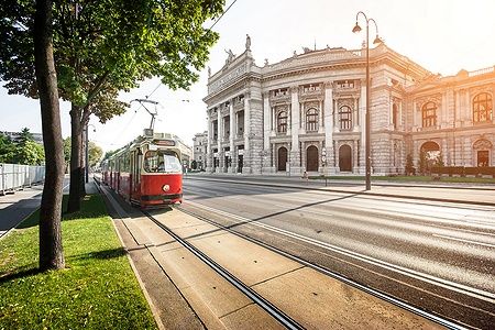 Tram rosso davanti al Burgtheater sulla Ringstrasse di Vienna al tramonto.