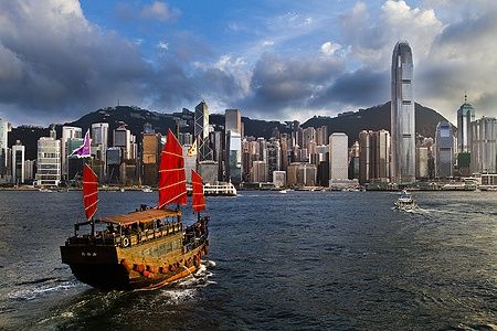 Giunca con vele rosse davanti alla skyline moderna di Hong Kong.