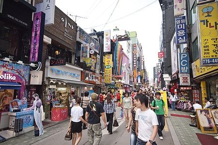 Persone che camminano nel vivace quartiere di Myeong-dong a Seoul, circondati da negozi.