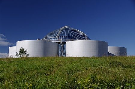 Il Perlan a Reykjavik sotto un cielo blu, con una cupola di vetro e prati verdi.