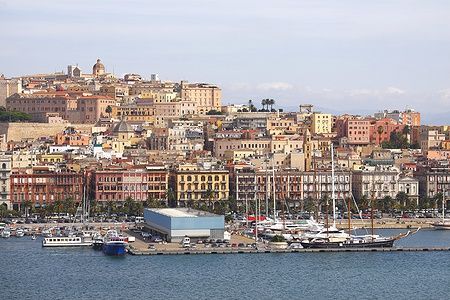 Vista del porto di Cagliari con imbarcazioni e edifici storici sullo sfondo.