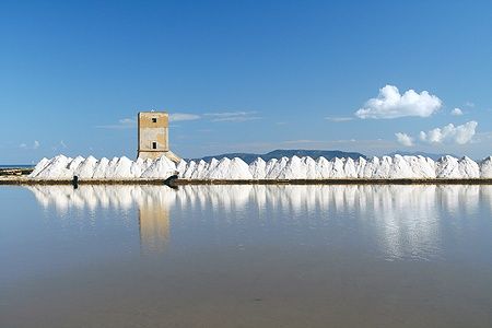 Saline di Trapani con Torre di Nubia e cumuli di sale riflessi nell'acqua.