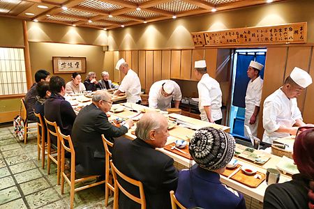 Interno del ristorante a Ginza Kyubey con chef in divisa che servono persone sedute lungo un bancone di legno.