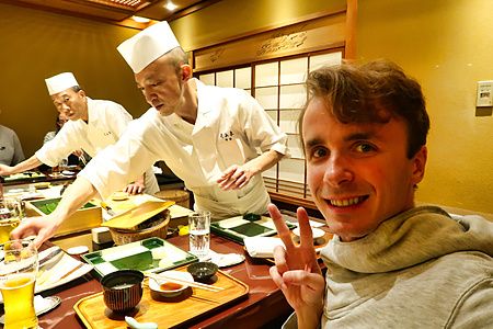 Marco Togni sorride col segno di pace mentre chef preparano sushi al Ginza Kyubey.