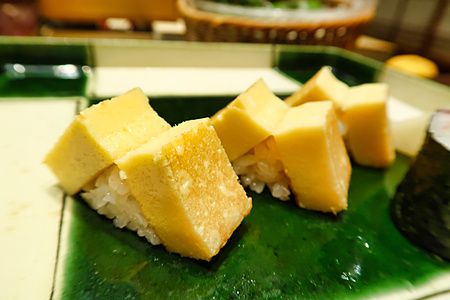 Tamagoyaki a Ginza Kyubey, fette di frittata giapponese su riso servite su un piatto di ceramica verde a Tokyo.