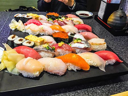 Piatto di sushi assortito su tavolo con persona in background.