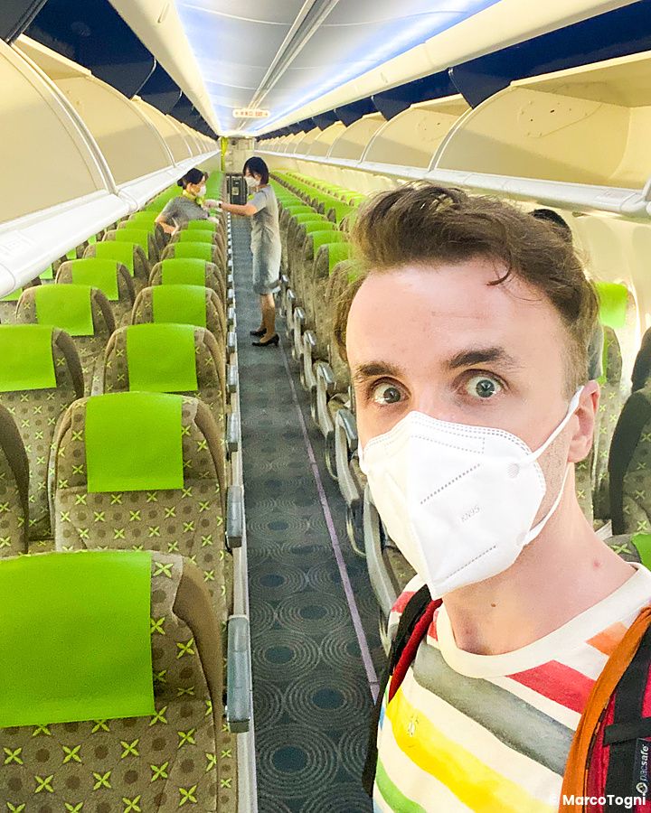 Marco Togni indossa una mascherina e si scatta un selfie nel corridoio di un aereo in Giappone con due assistenti di volo.