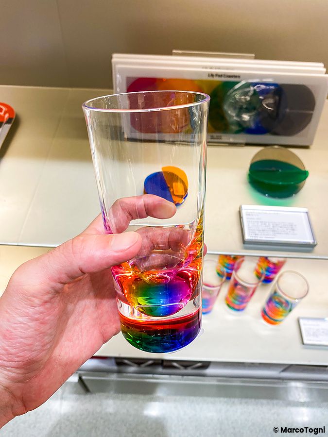 Una mano sostiene un bicchiere con base arcobaleno presso il Moma Design Store a Tokyo.