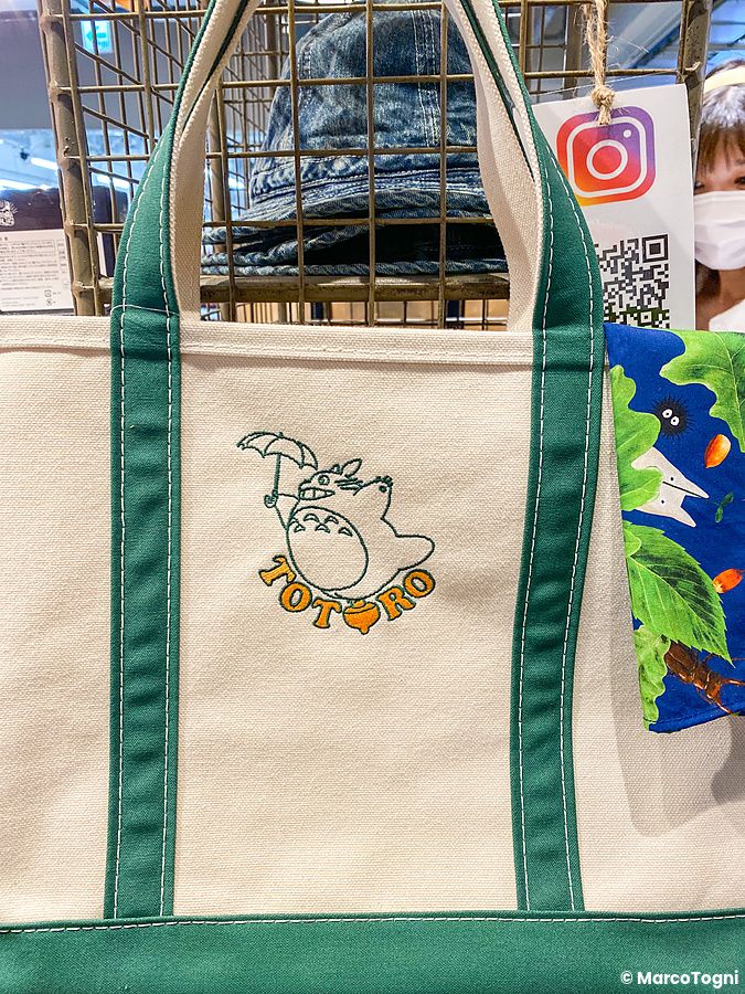 Borsa in tela con ricamo di Totoro esposta nel negozio di Studio Ghibli a Tokyo, con una persona sullo sfondo.