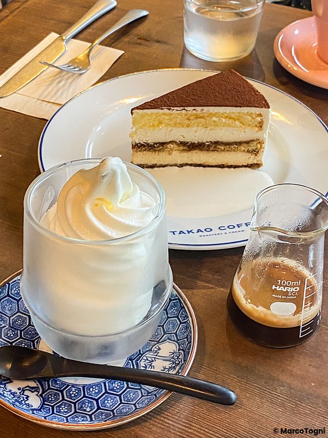 Una fetta di tiramisù, un gelato soft e un contenitore con caffè su un tavolo presso Takao Coffee.