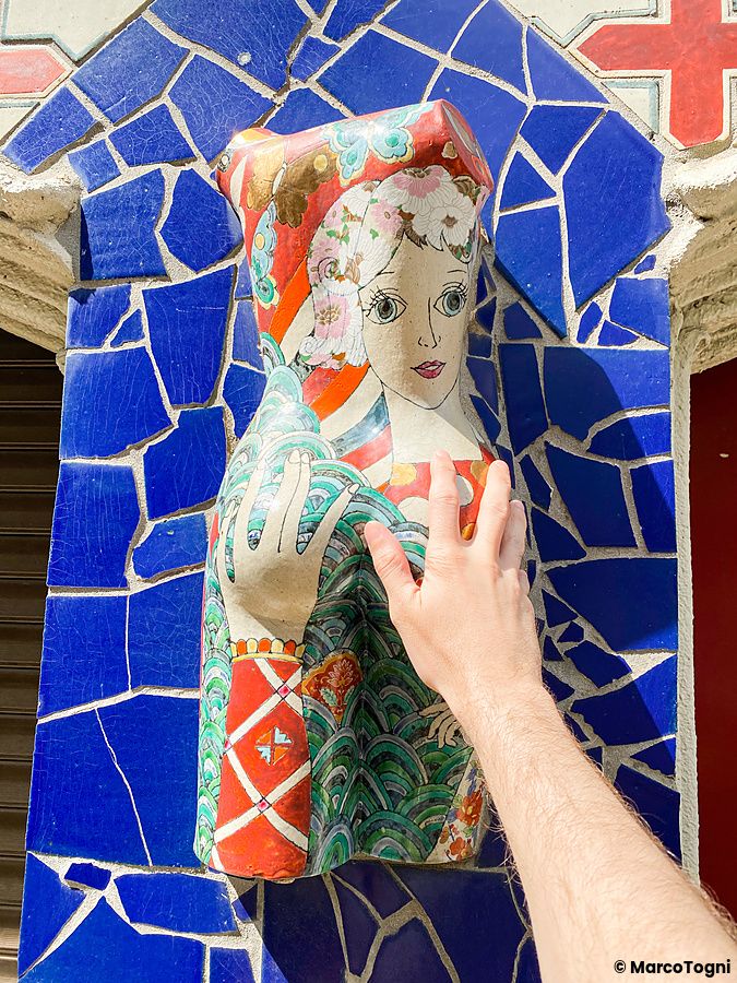 Una mano tocca una decorazione in ceramica raffigurante un volto di donna su una parete a mosaico blu presso El Dorado a W...