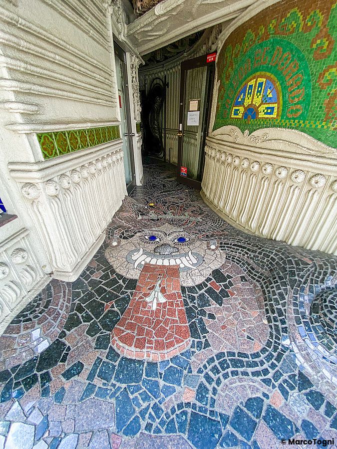 Ingresso dell'edificio El Dorado a Waseda caratterizzato da un pavimento a mosaico con volto grottesco e pareti decorate.