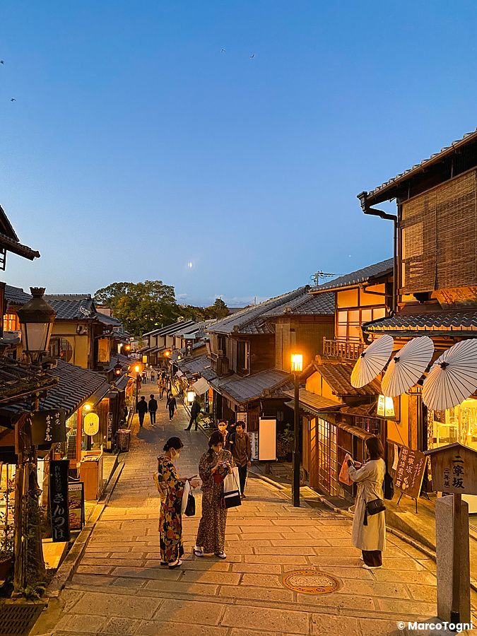 Strada tradizionale di Kyoto al tramonto con persone in kimono.