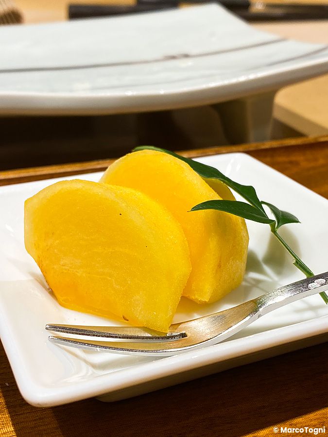 Fette di frutta gialla servite su un piccolo piatto quadrato bianco con una forchetta presso Ginza Kyubey a Tokyo.